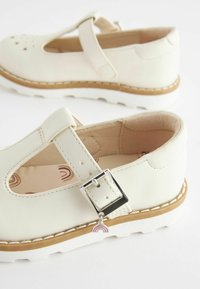 Białe skórzane buty Mary Jane z zapięciem na klamrę, okrągłym noskiem i teksturowaną gumową podeszwą, ozdobione tęczowym charms'em i miękką podszewką.