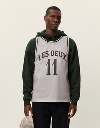 Hallhi võrdsed korvpallipluus halli sissetoomisega, millel on rohelised "LES DEUX" tekst ja number 11, kihtide kaupa tumerohelise kapuutsiga. Omab soonik-vasaku kaelus ja õlavarre alasid.