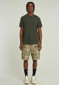 Olijf groene katoenen T-shirt met een ontspannen pasvorm, gecombineerd met camouflage cargoshorts met meerdere zakken en een gestructureerd patroon.