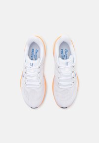 Paire de chaussures de sport blanches en mesh avec semelles orange, lacets blancs et semelles intérieures bleues marquées, vues de dessus sur fond blanc.