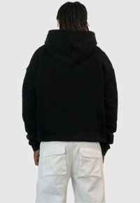 Svart hooded sweatshirt med avslappnad passform, med en stor huva och sänkta axlar, ihop med vita cargobyxor med klafffickor.