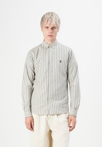 Langærmet skjorte i et lyst beige stof med mørkegrønne vertikale striber. Har en button-down krave og et broderet logo på brystet.