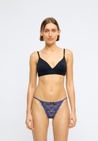 Schwarzer Triangel-Bralette mit dünnen Trägern und tiefem V-Ausschnitt. Marineblaue Spitzen-Tanga mit einer Schleife, die komplexe Blumenmuster und gewellte Kanten zeigt.