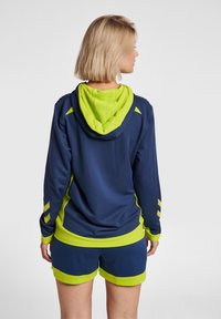 Felpa sportiva blu navy con cappuccio verde lime e dettagli in verde, caratterizzata da un design testurizzato, maniche corte e righe laterali sulle maniche e sui pantaloni.