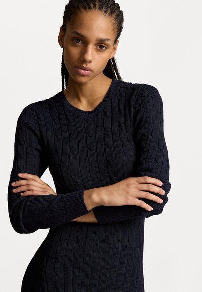 Pulover tricotat bleumarin cu un model de cablu, mâneci scurte și decolteu în V, expus pe un fundal simplu.