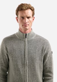 Grijze gebreide zip-up trui met een hoge kraag, een textuurpatroon en contrasterende accenten. Voorzien van een centrale rits en een logo-opdruk op de mouw.