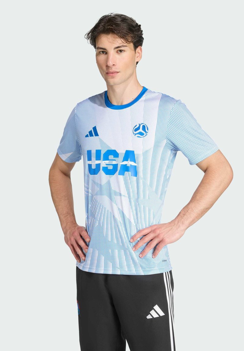 Modrá a bílá sportovní košile s krátkým rukávem a grafikou "USA", tečkovaným vzorem a logem; v kombinaci s černými kalhotami s bílými pruhy.