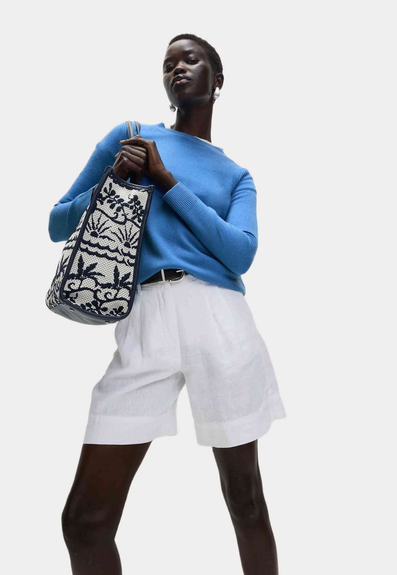 Modrý svetr, bílé lněné šortky a vzorovaná černobílá taška s květinovými vzory. Nosené s černým opaskem.