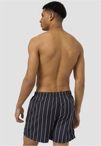 Shorts de bain rayés noir et blanc avec une taille élastique, tissu texturé, longueur mi-cuisse et poches latérales.