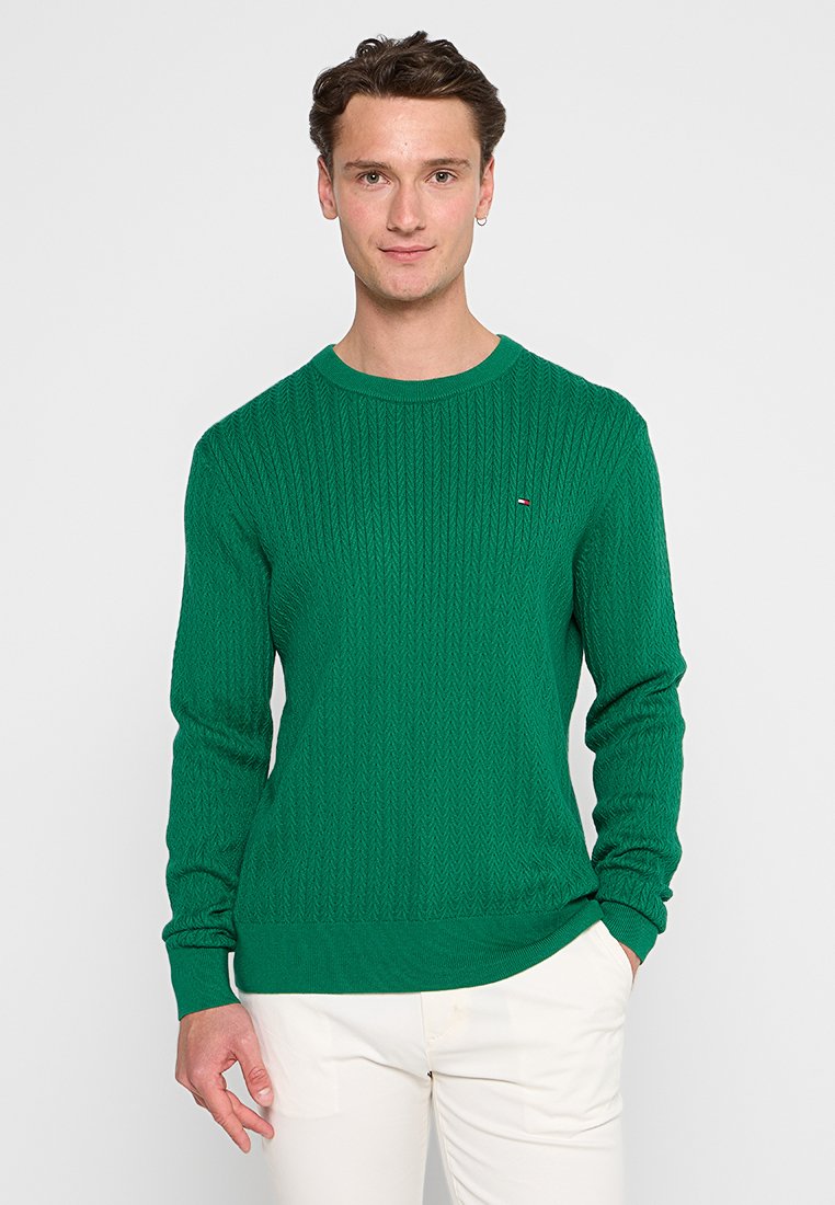 Groene gebreide trui met een ribbelstructuur, ronde halslijn en lange mouwen. Heeft een klein logo op de borst en een aansluitende zoom.