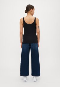 Svart ermeløs topp med rund rygg, kombinert med vide, mørkeblå jeans og hvite sneakers, med minimalistisk design.