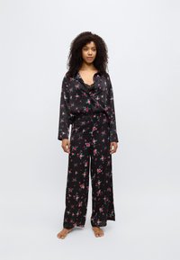 Ensemble de pyjama en satin noir avec motif floral, comprenant une chemise ample à boutons et un pantalon à jambes larges. Texture douce, coupe décontractée et manches longues.
