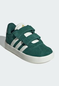 Scarpa da ginnastica verde in suede per bambini con accenti in pelle bianca, dotata di due cinturini in Velcro, punta rotonda e suola in gomma testurizzata.