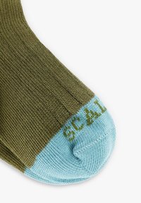 Acercamiento de un calcetín verde con la punta azul clara, que presenta la palabra "SCAL" tejida en la sección azul.