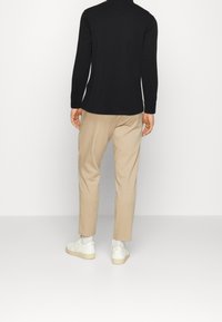 Svart långärmad skjorta, beige byxor och vita sneakers. Slät tygtextur, avslappnad passform och enkel design utan synliga mönster.