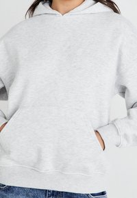 Ljusgrå hoodie i mjukt material, med en känguruficka, ribbade muddar och en justerbar huva. Avslappnad design och löst passform.