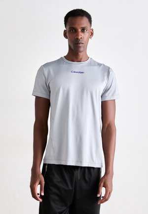 Light gray athletic t-shirt with short sleeves, round neck, and blue "Calvin Klein" logo. Material appears smooth with a subtle texture.