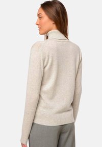 Pull à col roulé beige clair avec bords côtelés, fabriqué en tissu doux, présentant une coupe décontractée et des manches longues, vu de dos.