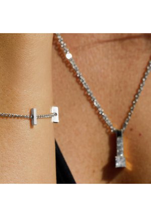 Collier et bracelet en argent avec un pendentif géométrique. La chaîne est finement maillée, présente des surfaces réfléchissantes et un design minimaliste, mettant en valeur l'élégance.