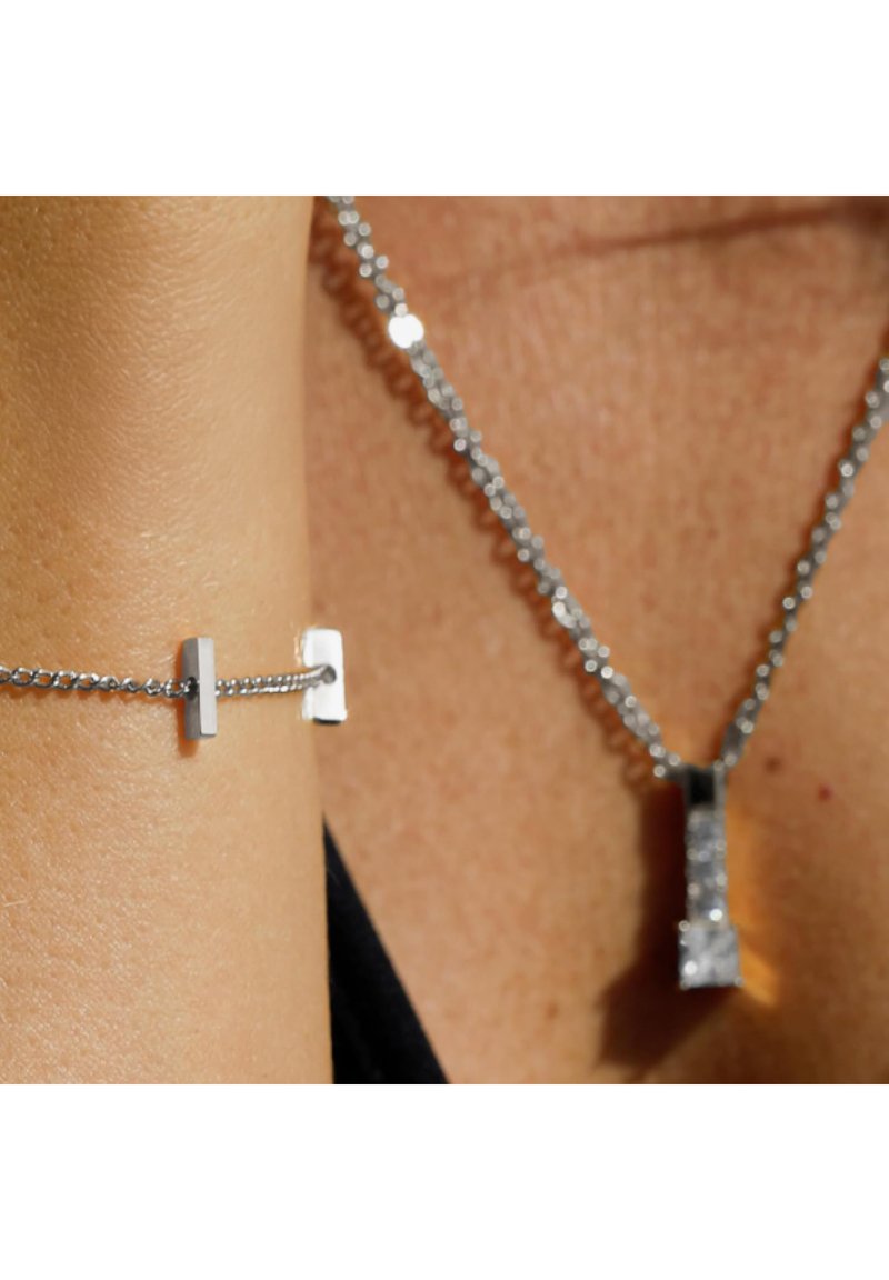 Silberne Halskette und Armband mit geometrischem Anhänger. Die Kette ist fein verlinkt und besitzt reflektierende Oberflächen sowie ein minimalistisches Design, das die Eleganz unterstreicht.