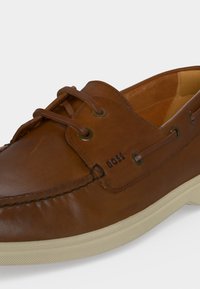Chaussure bateau en cuir marron avec lacets en cuir, coutures visibles, logo BOSS sur le côté et semelle en caoutchouc texturée blanc cassé.