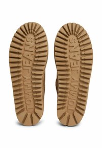 Suela de goma marrón con un patrón de tracción estriado y "TOMMY JEANS" en relieve, que presenta un diseño grueso y resistente para durabilidad y agarre.