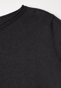 Chemise en coton noir avec un col rond, une texture à fine rainure et des coutures visibles sur la couture de l'épaule. Design simple et minimal.