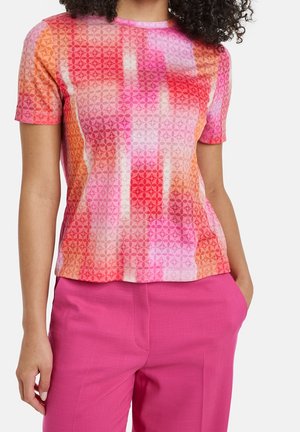 Top de manga corta en un tejido ligero y texturizado que presenta patrones geométricos en rosa, naranja y blanco, combinado con pantalones vibrantes en rosa.