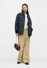 Giacca imbottita blu navy con bottoni dorati, top bianco, pantaloni beige a gamba larga con texture, ballerine nere e borsa bordeaux con tracolla a catena.