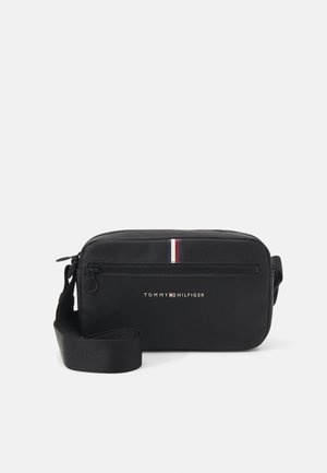 Czarna torebka na ramię wykonana z trwałego materiału, wyposażona w zamek błyskawiczny, regulowany pasek oraz czerwono-biało-niebieski akcent z przodu.