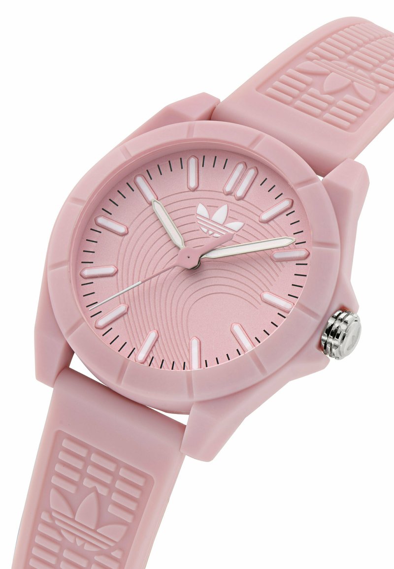 Montre en silicone rose avec un bracelet texturé, un boîtier rond, des accents argentés et un cadran à motifs présentant un logo et des marquages linéaires.