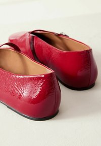 Red patent leather ballet flats with a rounded toe and a flat black sole; features a smooth texture and a subtle sheen.
