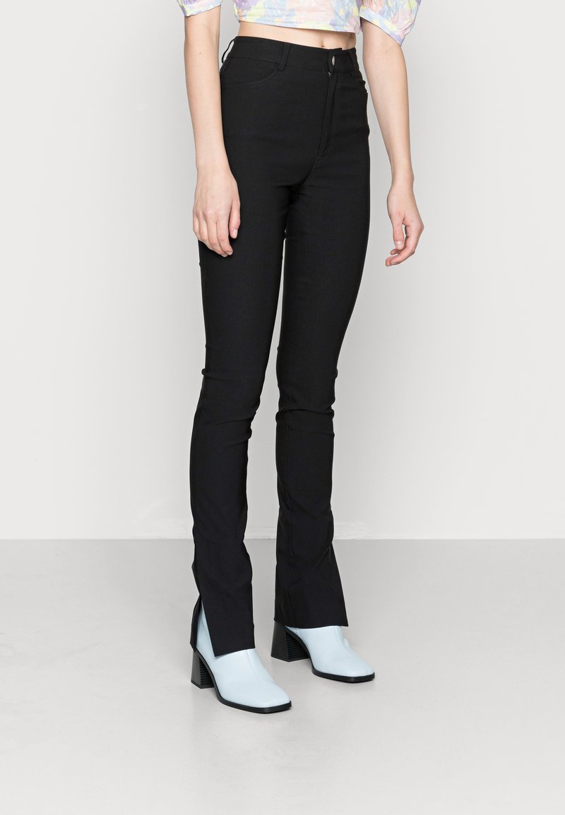 Jeans flare pretos de cintura alta com fecho frontal de zíper e botão. Combinados com botas de cano curto de salto de cor azul clara. Tecido suave, ajuste sob medida.
