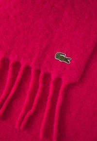 Scarf in lana di un vivace rosa, dalla consistenza morbida, con bordi frangiati e un piccolo logo ricamato di un coccodrillo verde.