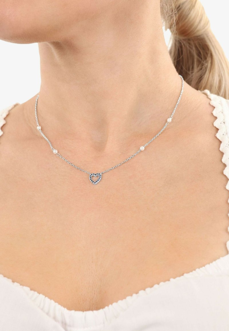 Collar de plata con un colgante en forma de corazón y pequeñas perlas a lo largo de la cadena, mostrando un diseño delicado sobre un fondo de tono de piel.