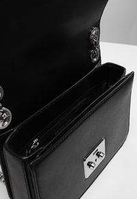 Borsa a mano in pelle nera con chiusura magnetica argento, tracolla a catena e compartimenti interni per l'organizzazione. Texture liscia e design elegante.