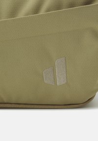 Bolsito en color verde oliva, hecho de tela texturizada, que presenta un logo prominente en gris claro en la parte frontal y un zipper de contraste a lo largo del borde inferior.
