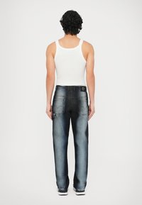 Temno modre kavbojke iz jeansa z bledenimi predeli, standardnimi zadnjimi žepi in usnjeno nalepko na pasu, združene z belim topom brez rokavov.