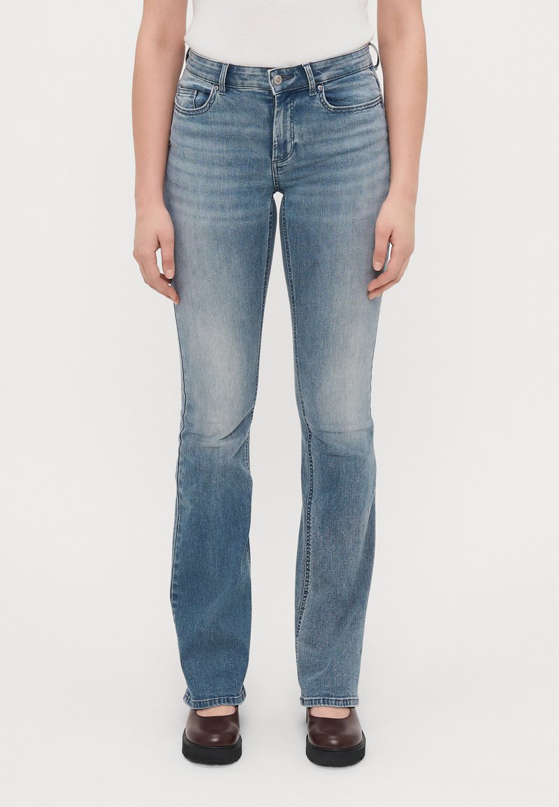 Világoskék farmernadrág, szélesített lábakkal, közép magas derékkal, öt zsebbel és finom koptatási részletekkel.