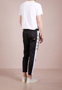 Schwarze Jogginghosen mit weißen Seitenstreifen und gelben Sternen, kombiniert mit einem schlichten weißen T-Shirt. Lässiger, lockerer Schnitt und leichtes Material.