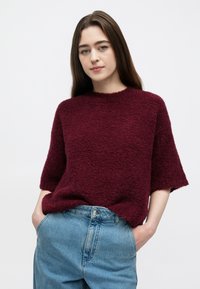Camisola de malha texturada burgundy com mangas curtas e decote redondo, combinada com jeans de ganga azul claro de cintura alta.
