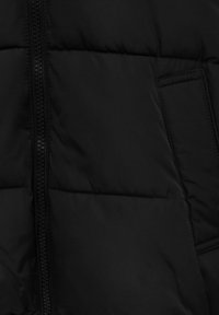 Svart uppblåsbar jacka med kviltad textur, som har en central dragkedja och sidoficka. Tyget verkar slätt och lätt.