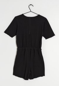 Black short-sleeve jumpsuit with an elastic waistband, zipper closure at the back, and scalloped hems on sleeves and shorts.