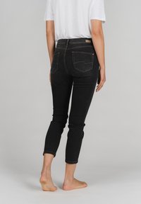 Schwarze Jeans aus Denim mit hoher Taille, verkürzter Länge und Fünf-Taschen-Design. Kontrastnähte und ein kleines Markenlabel auf der Rückseite.