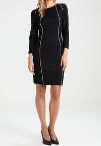 Czarna sukienka z rękawami trzyczwartowymi, z kontrastowym różowym przeszyciem wzdłuż szwów. Sylwetka typu bodycon, do kolan.
