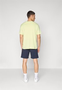 Lysegrønn t-skjorte med korte ermer kombinert med marineblå shorts. Modellen har på seg hvite joggesko og ankellange hvite sokker.