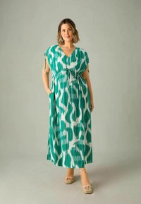 Robe maxi dans un motif abstrait vert et blanc, fabriquée en tissu léger. Dotée d'un décolleté en V, de manches courtes, d'une taille cintrée et de poches latérales.