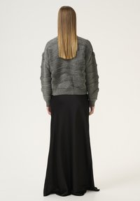 Szürke, texturált pulóver kiemelkedő mintákkal, hosszú fekete szoknyával társítva. Az outfiték sima, lágy vonalvezetésű.