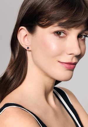 Złote kolczyki wkręty z okrągłym turkusowym kamieniem, prezentujące gładkie, wypolerowane wykończenie. Modelka ma proste brązowe włosy, a tło jest neutralne.