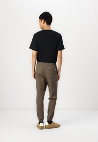 Czarny t-shirt z krótkim rękawem w połączeniu z brązowymi dresami na gumce; dresy mają tylną kieszeń oraz ściągacze na kostkach, w zestawieniu z beżowymi sneakersami.
